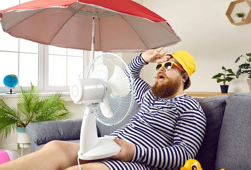 A man sitting inside with a fan and umbrella.