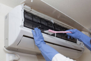 Homeowner wearing blue latex gloves cleaning indoor HVAC unit with a coil brush
