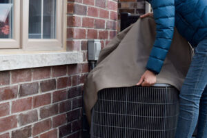 A person removing a cover from an outdoor HVAC unit.