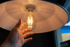 Hand reaching for lit light bulb in lamp