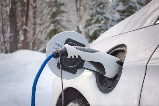 An electric vehicle charging outside with snow and trees in the background.