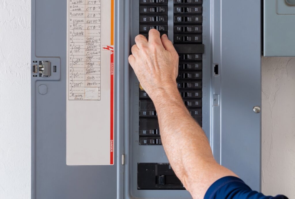 A man flipping a circuit breaker on an electrical panel.