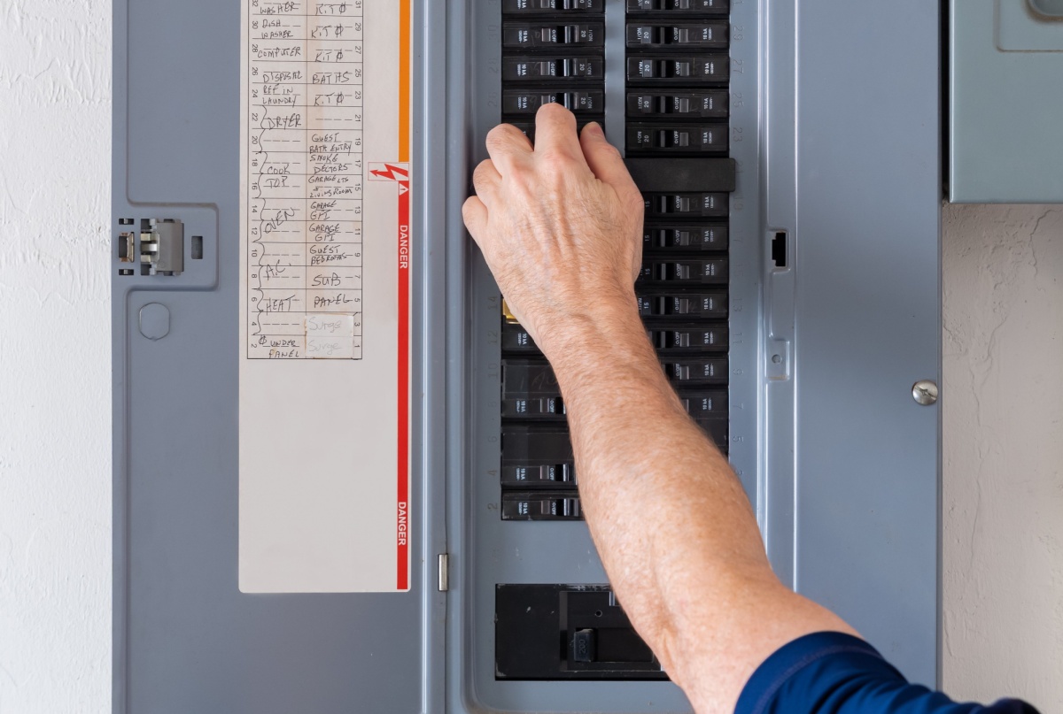 A man flipping a circuit breaker on an electrical panel.