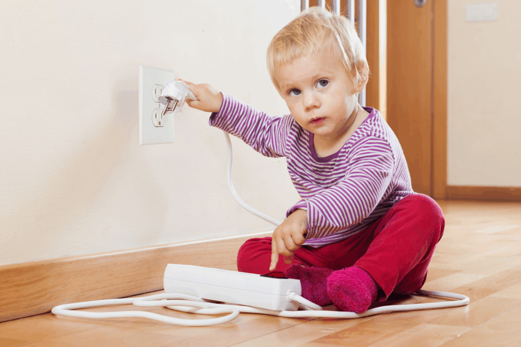 Baby holding an electrical cord near an outlet.
