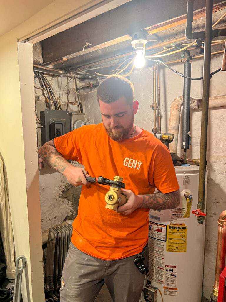 GEN3 Electric & HVAC technician Kyle working on a boiler installation in Philadelphia, adjusting a brass heating component with a wrench.