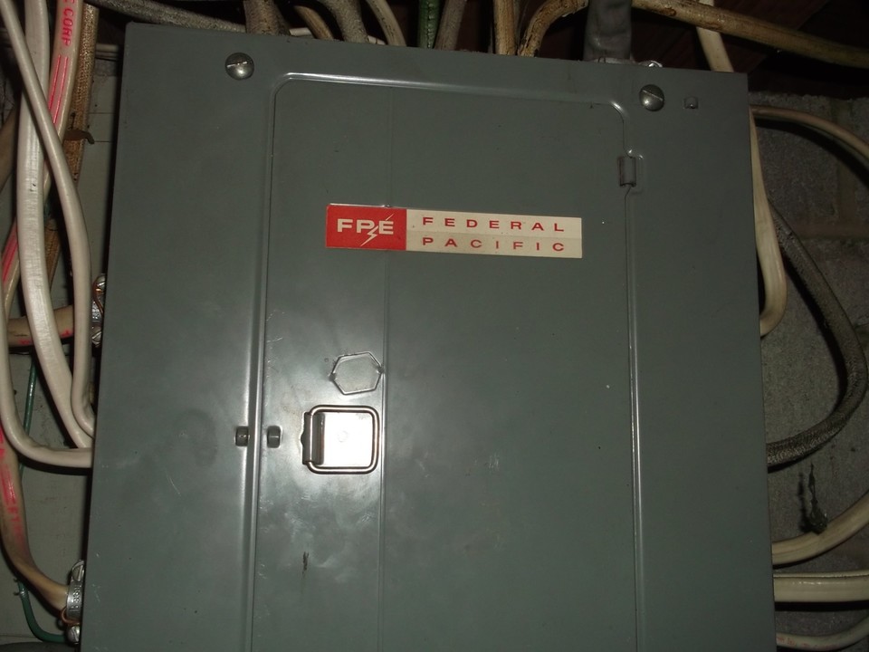 Federal Pacific Electric (FPE) Stab-Lok breaker panel with gray metal cover and red logo, a mid-20th-century electrical panel known for breaker failure and fire risk in older homes.
