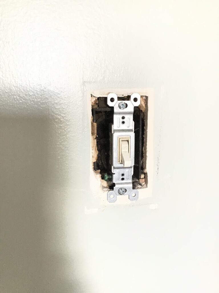 Exposed light switch without cover plate showing recessed electrical box and unfinished wall cutout before repair during a Philadelphia electrical rewire.