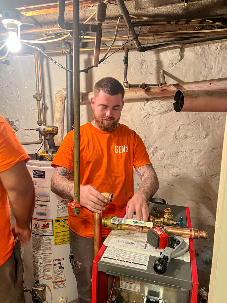 GEN3 HVAC technician working on a boiler or hot water heater system in a basement, reinforcing local boiler expertise