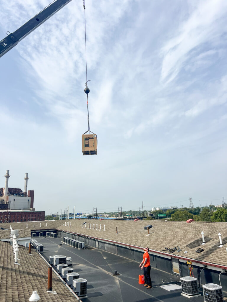 Crane lifting a new high-efficiency rooftop AC unit during installation by GEN3 Electric & HVAC in Philadelphia, with technician guiding the process.