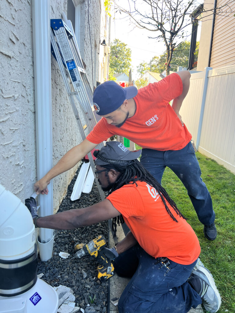 GEN3 Electric & HVAC technicians Eric and Cush installing protective PVC linehide during a Mitsubishi ductless mini-split installation in Roxborough, Philadelphia, ensuring clean, secure, and weather-protected refrigerant line placement.