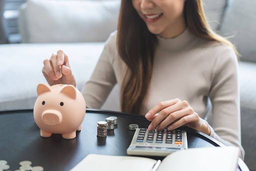 Homeowner putting money in piggy bank as she calculates bills.